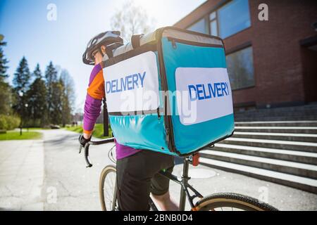Femme dans un casque avec un grand sac à dos de livraison de nourriture à vélo dans la rue. Jour de printemps ensoleillé dans la ville. Portrait d'une femme de messagerie sur un vélo Banque D'Images