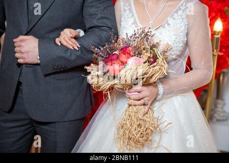 La mariée est entrée dans l'aisselle du marié et a tenu un bouquet de fleurs . corail séché atteindre le blé rose coton fleur bouquet de mariée . Banque D'Images