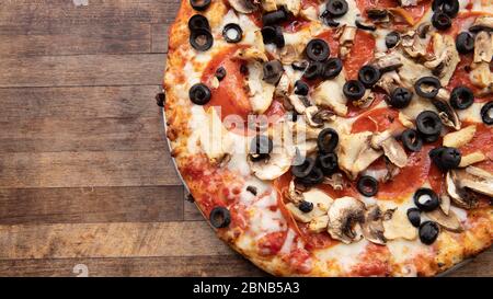 Pizza surmontée d'olives, de champignons, de pepperoni et de fromage sur une planche à découper décorative. Banque D'Images