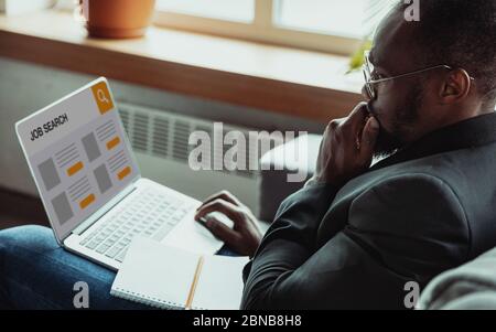 Homme à la recherche d'un emploi pendant la crise mondiale. Trouver un emploi en ligne. Concept d'affaires, Internet et de réseautage. L'homme caucasien regarde par les postes vacants et envoie des CV, a besoin de gagner. Barre de recherche moderne. Banque D'Images