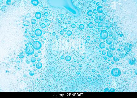 Gros plan mousse blanche avec bulles à la surface de l'eau, lessive en poudre avec savon et bain bleu, bulle transparente de fond abstrait. Banque D'Images