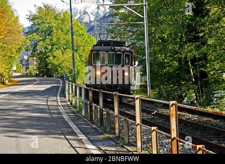 Belle photo d'un train en cours de course sur un rail à côté une route autour des arbres Banque D'Images