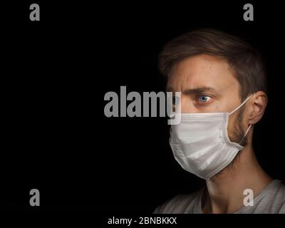 Bleu-yeux jeune homme blanc portant un masque et des vêtements décontractés, à l'air déterminé. Banque D'Images