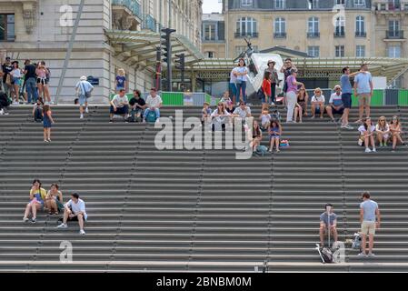 Paris, France. Touristes et habitants assis sur les marches des escaliers en bois sur la rive sud de la Seine, près du Musée d'Orsay. Banque D'Images