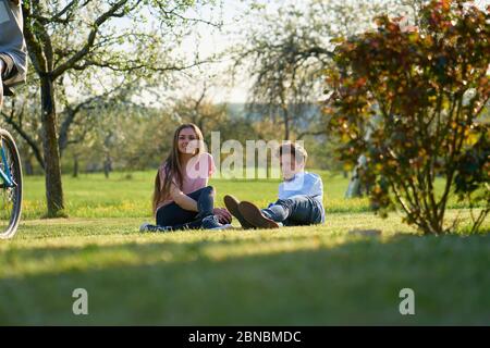 Jeune couple faisant une pause dans le pays en Allemagne, en se posant sur le sol sur un pré, en prenant soin d'un cycliste, vous pouvez voir des arbres et des buissons Banque D'Images