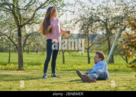 Jeune couple sur un pré entre pommiers au printemps riant heureux les uns aux autres et s'amusant Banque D'Images