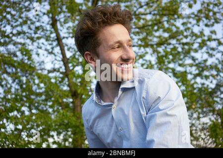 Portrait d'un jeune beau rire heureux homme regardant par-dessus son épaule dans la belle verdure Banque D'Images