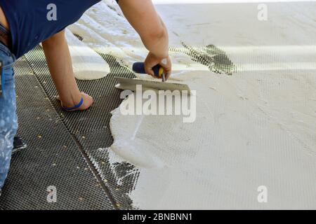 Un ouvrier de la construction truroweling mortier sur un sol en béton en préparation pour la pose de carreaux de plancher. Banque D'Images