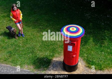 Loughborough, Leicestershire, Royaume-Uni. 14 mai 2020. Une fille passe son chien devant une boîte postale du Royal Mail qui a été bombardée de fils de couleurs arc-en-ciel pour montrer son soutien aux travailleurs clés pendant le confinement en cas de pandémie du coronavirus. Credit Darren Staples/Alay Live News. Banque D'Images