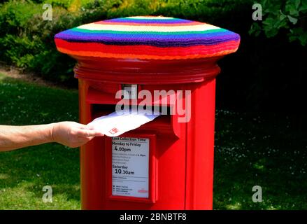 Loughborough, Leicestershire, Royaume-Uni. 14 mai 2020. Une femme posta une lettre dans une boîte postale du Royal Mail qui a été bombardée de fils de couleurs arc-en-ciel pour montrer son soutien aux principaux travailleurs pendant le confinement en cas de pandémie du coronavirus. Credit Darren Staples/Alay Live News. Banque D'Images