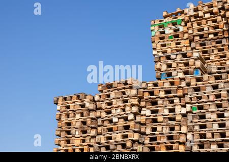 Palettes de marchandises en bois pour le stockage et le transport de marchandises et de marchandises empilées les unes sur les autres par un grand mur contre un ciel bleu clair. Banque D'Images