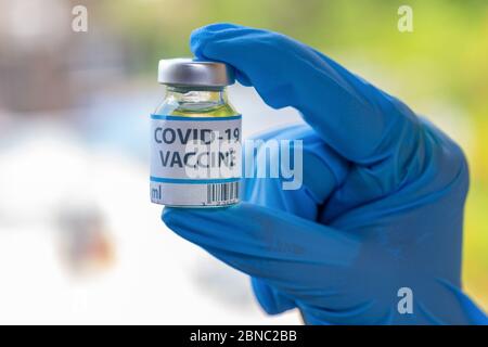 Main portant des gants médicaux en gros tenant une bouteille de vaccin utilisée pour le traitement des patients Covid-19 Banque D'Images