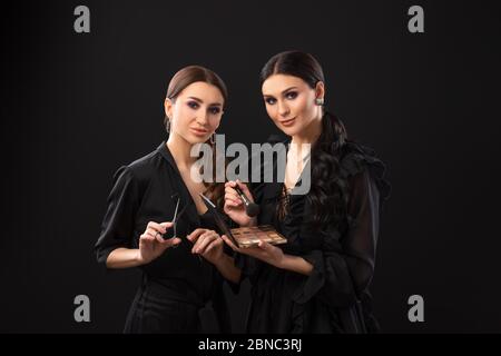 deux filles en robes foncées sur fond noir. Maquilleur et coiffeur avec ses propres outils de travail Banque D'Images