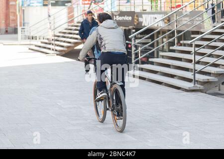 Novosibirsk, Russie - 04.26.2020 : un homme dans un pantalon noir et une veste grise fait un vélo pour travailler sur des dalles le long du bâtiment du centre d'affaires Banque D'Images