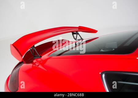 Gros plan d'un aileron sur une voiture moderne rouge sous les lumières isolées sur un fond gris Banque D'Images