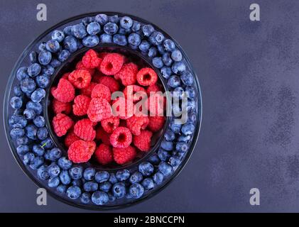 Framboises et bleuets biologiques frais sur fond sombre. Banque D'Images