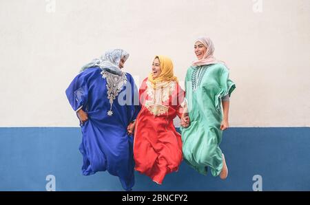 Les femmes musulmanes heureuses ayant le plaisir de sauter et rire ensemble en plein air - gens style de vie et culture concept de religion - fond blanc et bleu Banque D'Images