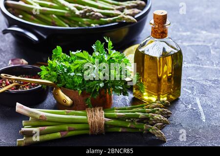 gros plan d'un bouquet d'asperges vertes fraîches avec plat à pâtisserie noir, bouteille d'huile d'olive à l'arrière-plan, vue horizontale depuis le dessus Banque D'Images