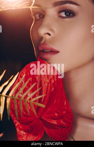 Portrait d'une femme avec un anthurium rouge et une fougères en regardant l'appareil photo sur fond sombre Banque D'Images