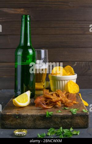 Calmar péruvien avec bière, citron et chips de pomme de terre sur un panneau en bois sombre. En-cas sur le poisson avec de la bière. Gros plan Banque D'Images