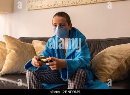 Pendant la pandémie du COVID-19, le garçon joue à la maison avec une console Banque D'Images