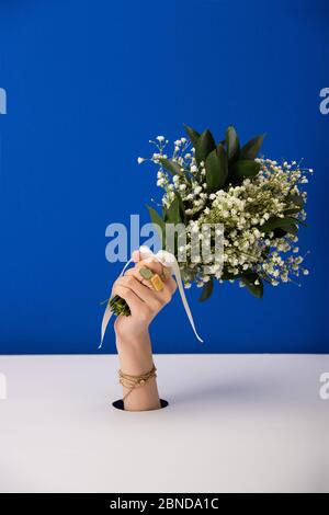 vue courte de la femme avec bracelet tenant un bouquet de petites fleurs printanières isolées sur le bleu Banque D'Images