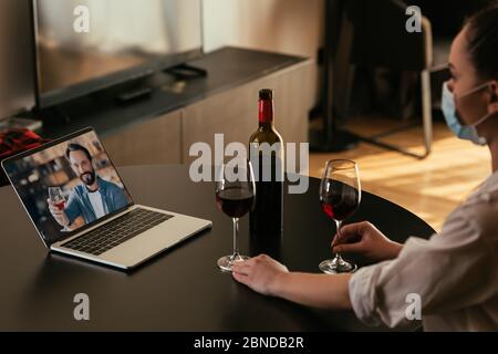 attention sélective de la jeune femme dans le masque médical ayant chat vidéo avec le petit ami près des verres et une bouteille de vin rouge Banque D'Images