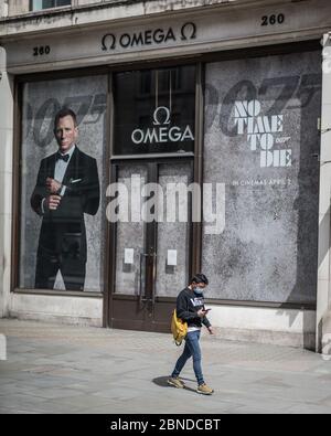 Une personne dans un masque facial marche à côté du panneau « No Time to Die » James Bond sur un Regent Street déserté à Londres pendant le confinement. Banque D'Images