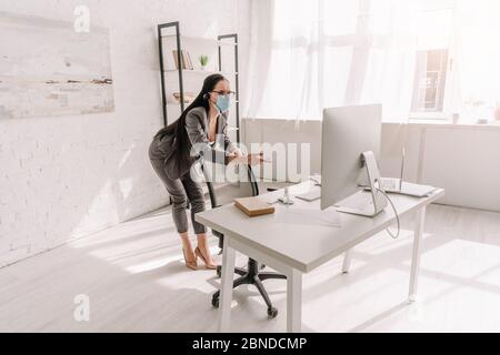 jeune femme d'affaires en tenue formelle et masque médical pointant avec le doigt sur l'écran d'ordinateur à la maison Banque D'Images