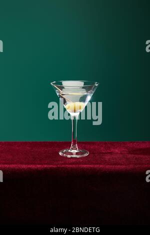 Verre à cocktail en cristal avec vermouth et olive entière sur cure-dent isolé sur vert Banque D'Images