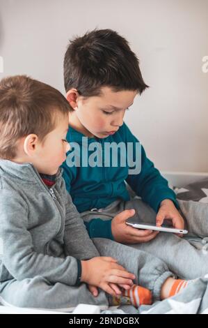 POZNAN, POLOGNE - 18 avril 2020 : deux jeunes garçons polonais de race blanche utilisant un comprimé assis sur un lit. Banque D'Images