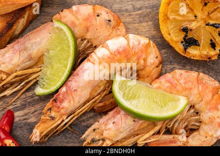 vue rapprochée des crevettes frites avec citron, piment et citron vert sur panneau de bois Banque D'Images