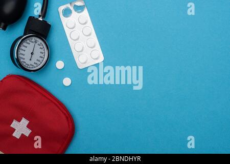 vue de dessus de la trousse de premiers soins, des comprimés dans un blister et un sphygmomanomètre sur fond bleu Banque D'Images