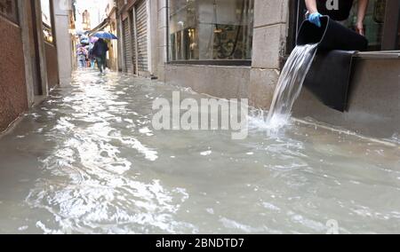 Personne vidant l'intérieur de la boutique inondé après l'inondation à Venise et l'allée étroite couverte d'eau de mer Banque D'Images