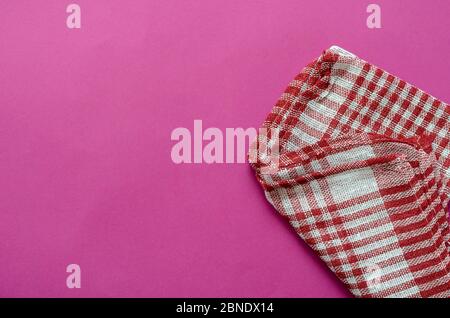 Fond rose clair avec une serviette à carreaux blanche et rouge. Serviette de cuisine pliée sur une table de couleurs. Arrière-plan minimaliste pour le multitâche. Vue de Banque D'Images