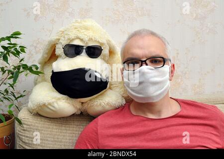 Un homme dans un masque médical avec un chien jouet est isolé à la maison. Concept de prévention des coronavirus Banque D'Images