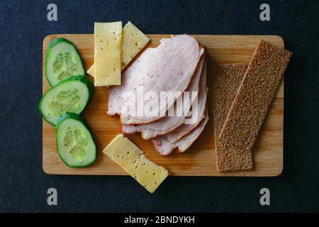 Trancher du jambon de viande, des concombres, du fromage et des pains à la gouvernail sur une planche en bois. Vue de dessus Banque D'Images