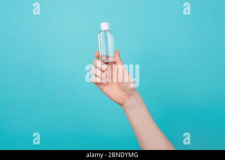 Concept de santé. Photo rognée d'une femme tenant une petite bouteille de désinfectant pour les mains isolée sur fond bleu turquoise sarcelle Banque D'Images