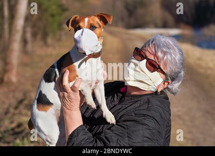 Femme âgée âgée avec un masque facial virus tenant son chien terrier Jack Russell aux mains, elle porte également un respirateur simple en tissu. Les animaux de compagnie sont probablement n Banque D'Images