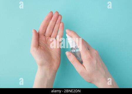 Garder les mains libres. Vue du dessus de la tête photo rognée d'une femme appliquant un désinfectant pour les mains en aérosol isolé sur fond turquoise Banque D'Images