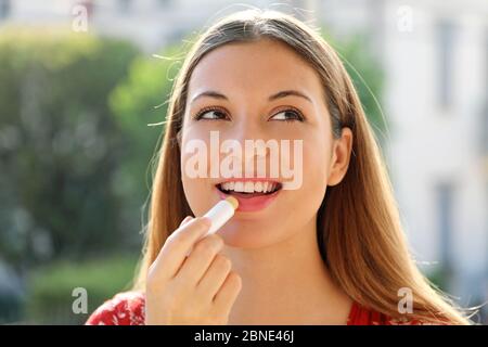 Portrait d'une jeune femme heureuse appliquant le baume à lèvres en été à l'extérieur Banque D'Images