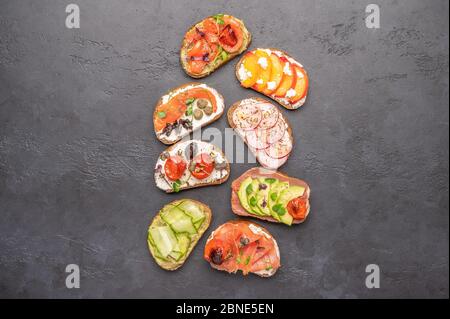 Sandwichs maison avec pain et divers ingrédients et épices sur fond sombre. Une nourriture saine et délicieuse pour le petit déjeuner et le déjeuner Banque D'Images