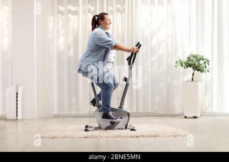 Jeune femme en surpoids à vélo d'exercice à la maison Banque D'Images