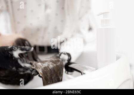 Bouteille de plastique blanc gros plan pour shampooing, femme de fond se lave la tête dans le salon de beauté. Concept cuir chevelu pour la calvitie, la coloration Banque D'Images