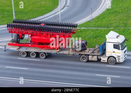 Transport de grandes machines agro-complexes pour la culture et le semis de cultures sur de longues remorques par camions le long de l'autoroute dans la ville Banque D'Images