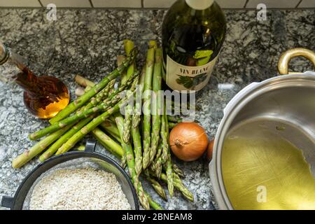 Cuisson d'un peu de riz risotto avec asperges, oignons et vin blanc. Faire la poêle avec de l'huile d'olive sur fond de granit. Vue grand angle. Banque D'Images