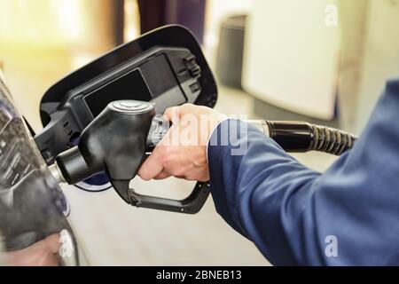 Homme d'affaires ravitailler sa voiture. Gros plan d'une main de homme en bleu en costume remplissant la voiture avec une pompe à gaz. Banque D'Images