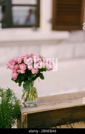 Réception de table de mariage. Un bouquet de roses roses dans un vase transparent en verre avec de l'eau, se dresse sur une boîte en bois contre le fond d'un Banque D'Images