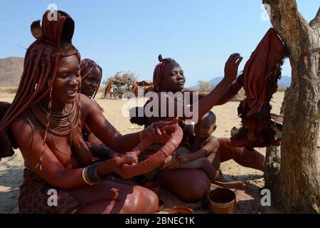 Femme Himba appliquant Otjize (un mélange de beurre, d'ocre et de frêne) sur des jupes faites de peau de chèvre et sur un collier. Vallée de Marienfluss. Kaokoland, Namib Banque D'Images