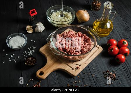 Hacher la viande hachée crue avec les ingrédients sur une table en bois noir. Cuisine maison. Banque D'Images
